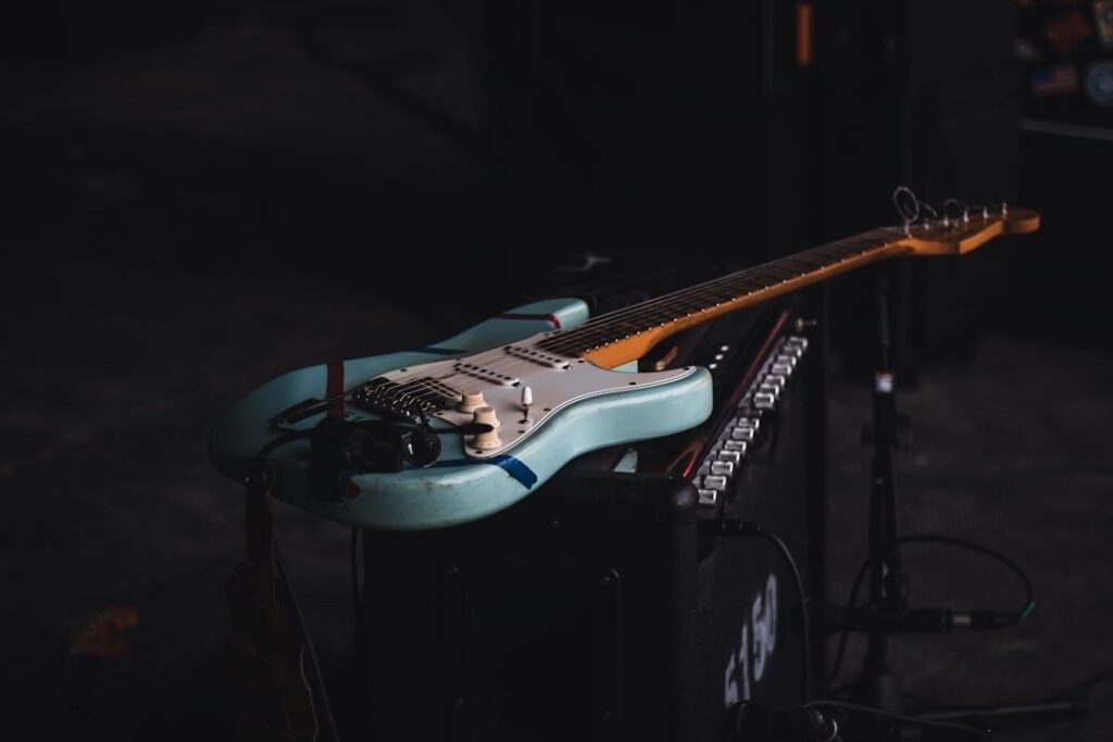 Blue electric guitar resting on audio equipment in a dark setting