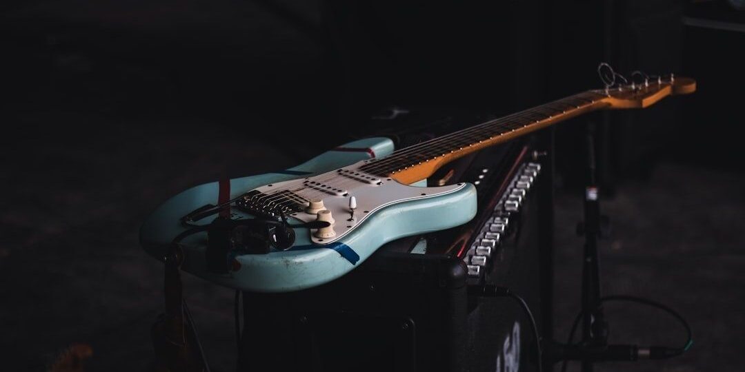 Blue electric guitar resting on audio equipment in a dark setting
