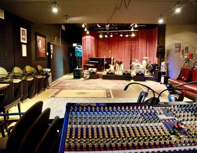 Small music venue with lit stage, drum kit, and mixing console